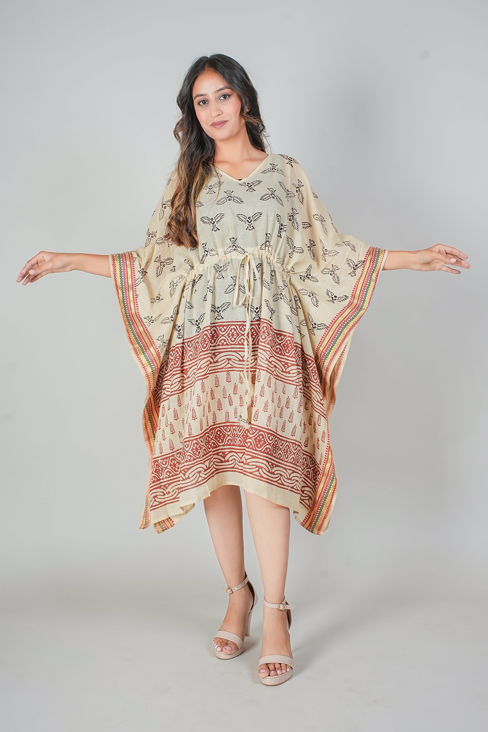 Woman wearing a patterned caftan dress with open sleeves on a creamy background