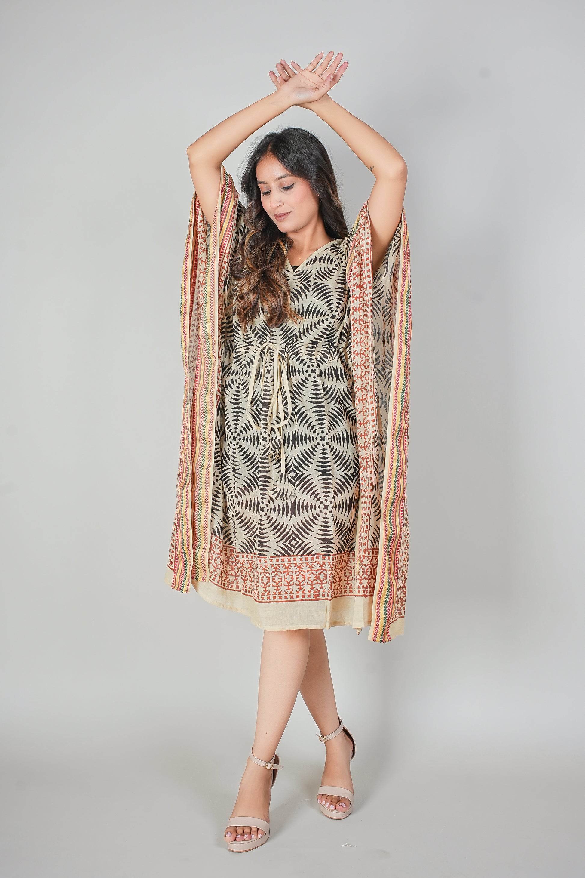 Woman wearing a patterned kaftan dress with a scarf draped over her shoulders against a gray background