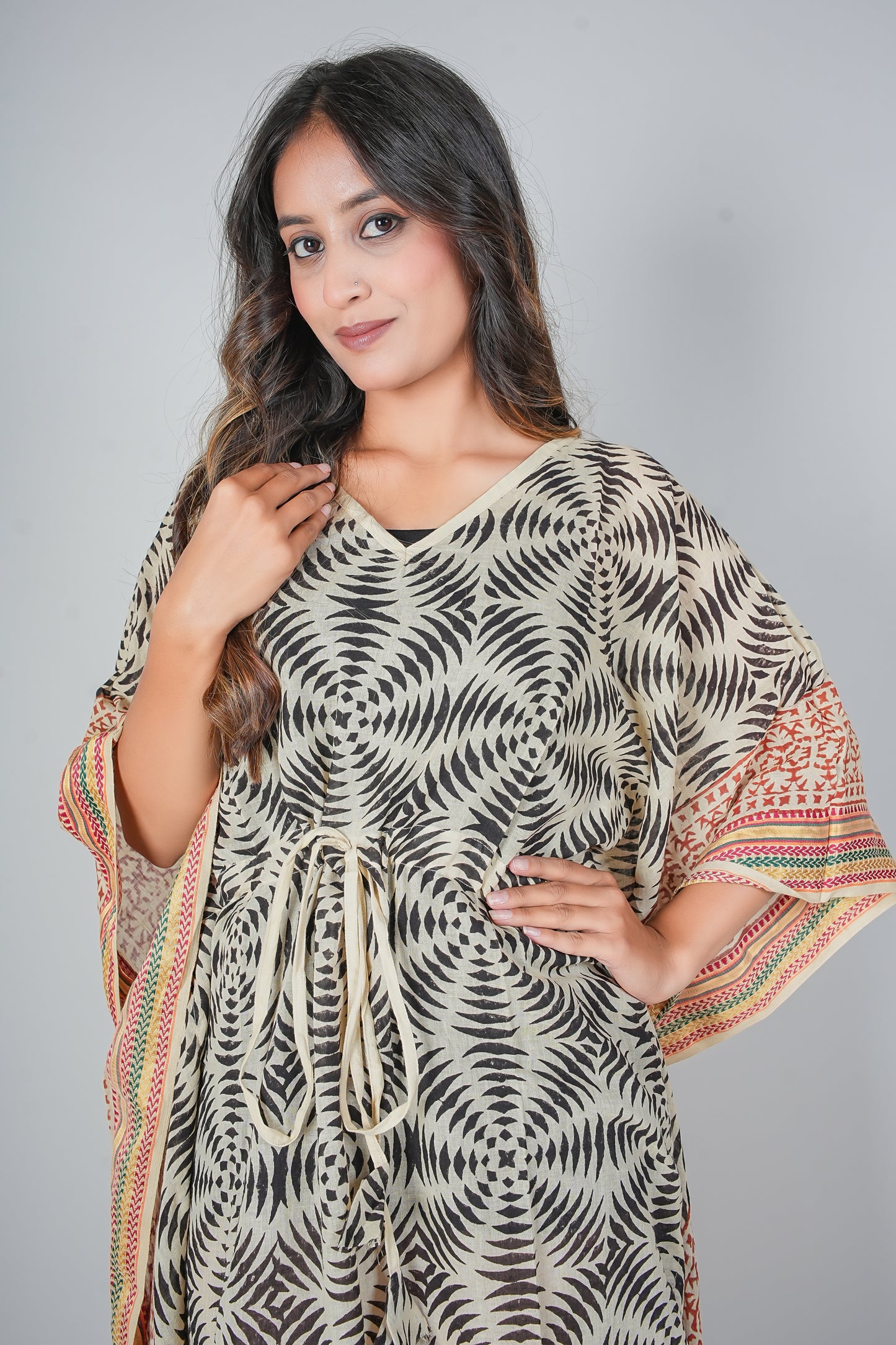 Woman wearing a patterned kaftan dress with colorful sleeves against a gray background